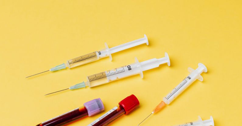 COVID Recovery - From above of plastic medical syringes without needle protective covers placed near filled clinical blood collection tubes on yellow background