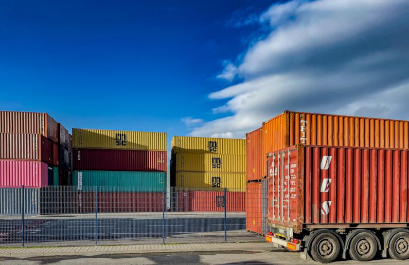 Infrastructure Economy - a truck is parked in front of a bunch of shipping containers