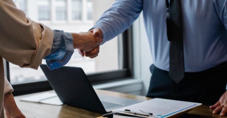 Contract Document - Crop unrecognizable coworkers in formal wear standing at table with laptop and documents while greeting each other before meeting