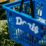 Buyer's Market - Side view of crop faceless buyer in casual clothes carrying shopping basket while choosing assorted colorful bell peppers in supermarket