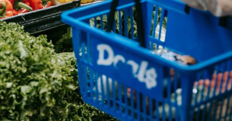 Buyer's Market - Side view of crop faceless buyer in casual clothes carrying shopping basket while choosing assorted colorful bell peppers in supermarket