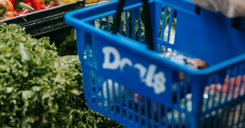 Buyer's Market - Side view of crop faceless buyer in casual clothes carrying shopping basket while choosing assorted colorful bell peppers in supermarket