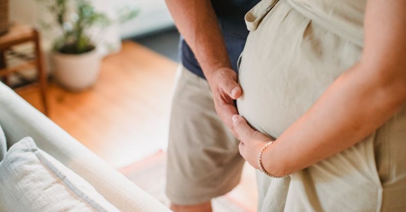 Future Home - From above of crop faceless couple in casual outfit standing in light living room and touching pregnant belly gently
