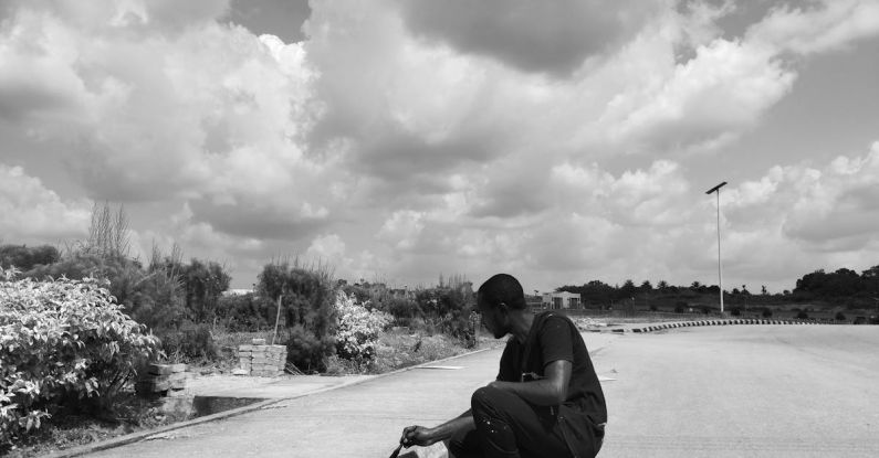 Curb Appeal - A man kneeling on the ground with his skateboard