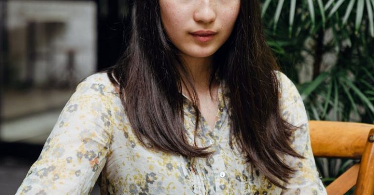 Newsletter - Young attentive Asian woman messaging on mobile phone in street cafe