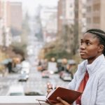 Student Housing - Contemplative ethnic student with journal on urban bridge