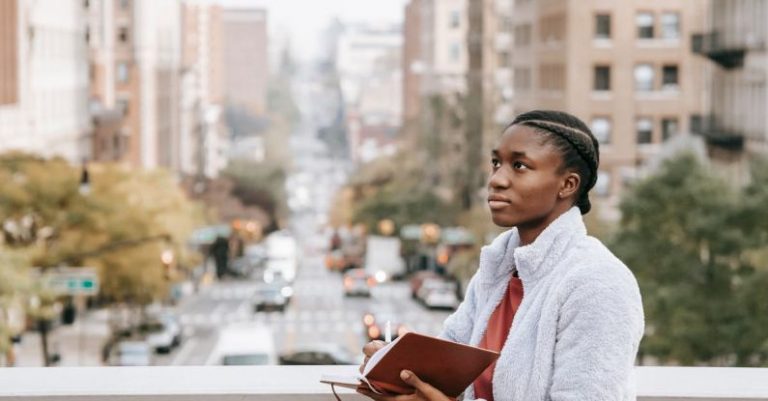 Student Housing - Contemplative ethnic student with journal on urban bridge