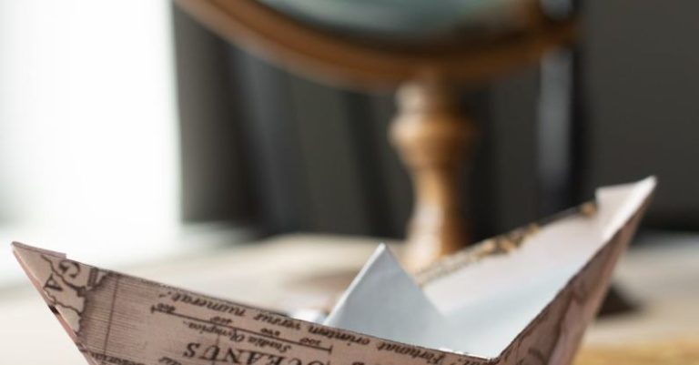 International Home - Paper boat made of world map placed on brown wooden table near round globe with continents in light room at home