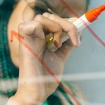 Financial Analysis - Woman in a Beige Coat Writing on a Glass Panel Using a Whiteboard Marker