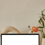 Property Portfolio - Netbook with white screen placed on shelf near uneven curved ceramic vases with flowers with green leaves near pipes in light room with white wall