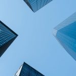 Infrastructure Economy - Low angle of high business towers with glass mirrored windows located in megalopolis downtown against blue sky