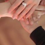 Community Meeting - Top view of faceless friends in different clothes stacking hands together while standing on wooden floor indoor on sunny day