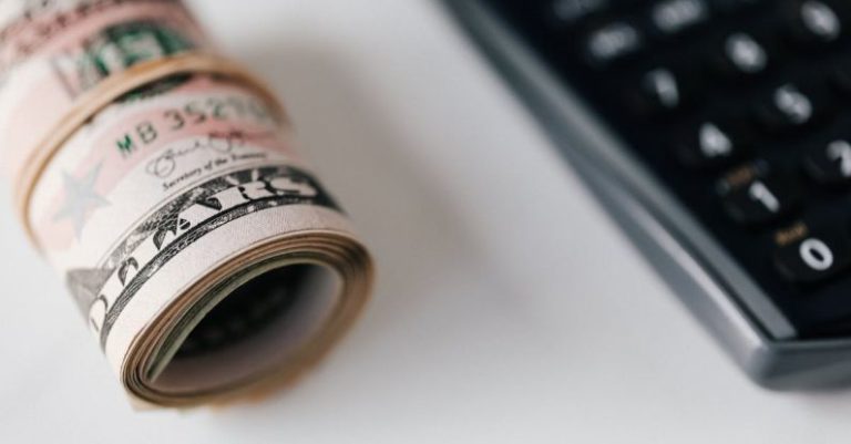 Electronic Signature - From above closeup of plastic calculator with number symbols on buttons near roll of American paper money tied with rubber band